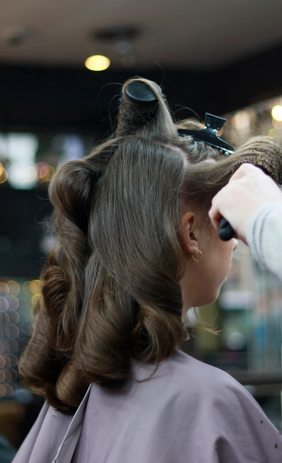 Hairstylist curling hair with professional styling tool in salon