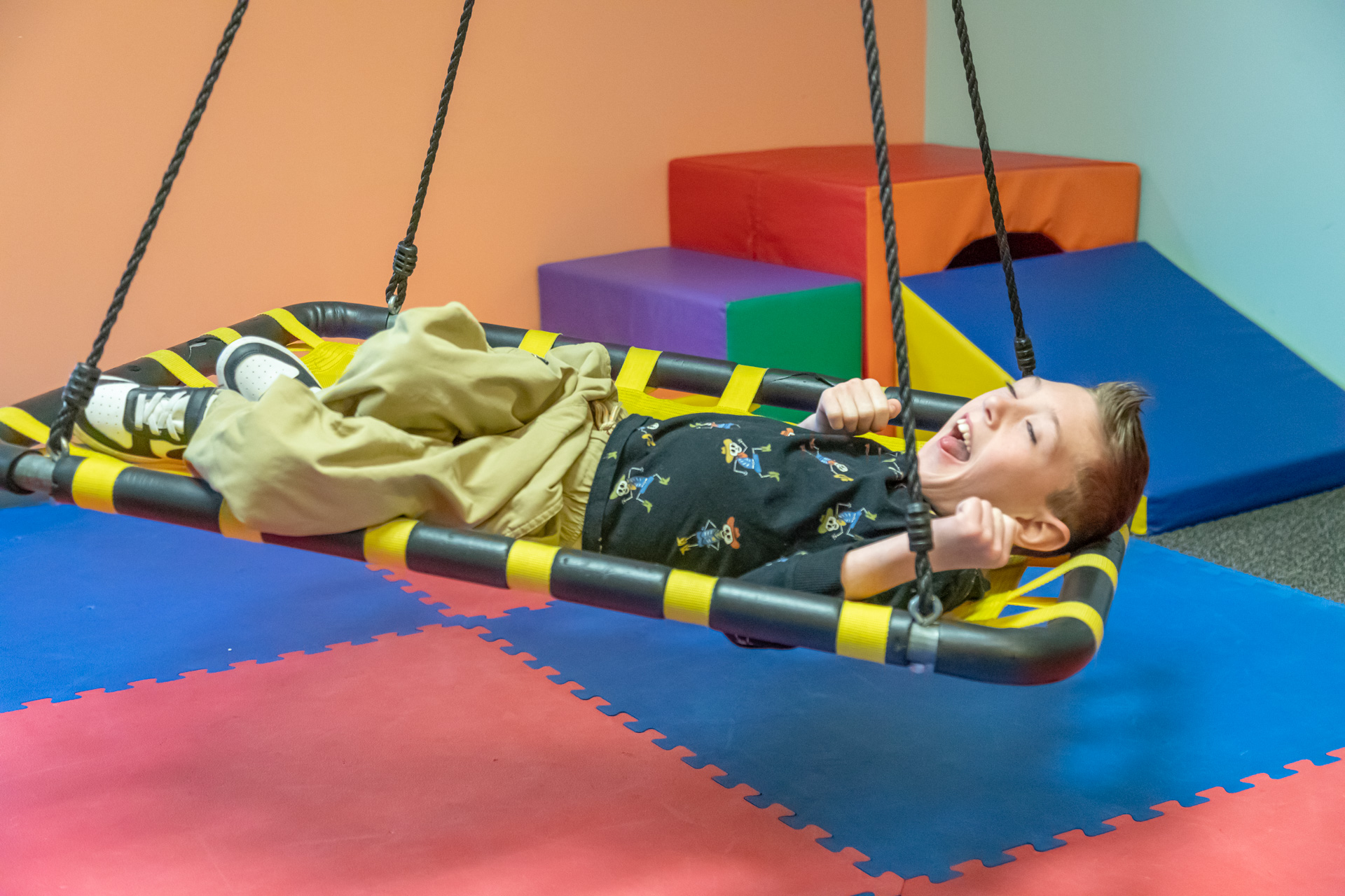 Child enjoying a sensory swing in a pediatric therapy gym, building balance and body awareness through play.