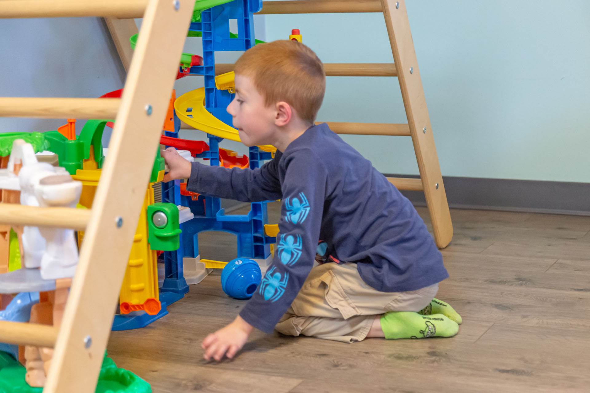 Child engaging in focused play with a multi‑level toy structure, practicing sensory regulation, problem‑solving, and early emotional resilience skills in a therapy setting