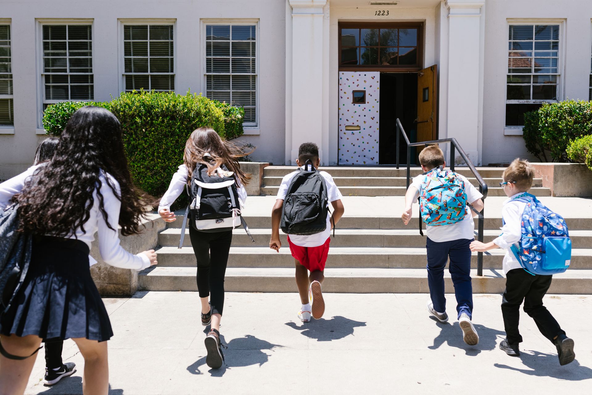 School‑age children with backpacks head toward a school building, illustrating confident back‑to‑school transitions supported by routine and preparation.