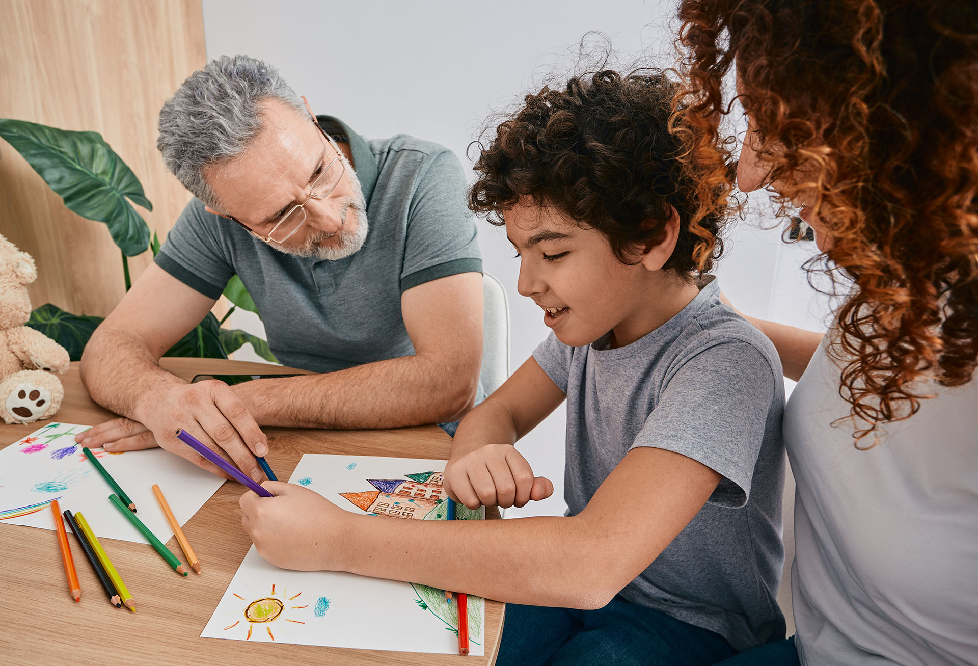 Parent, child, and therapist engaged in a playful drawing activity, illustrating how ABA therapy builds communication, social skills, and confidence through supportive, hands‑on interaction.