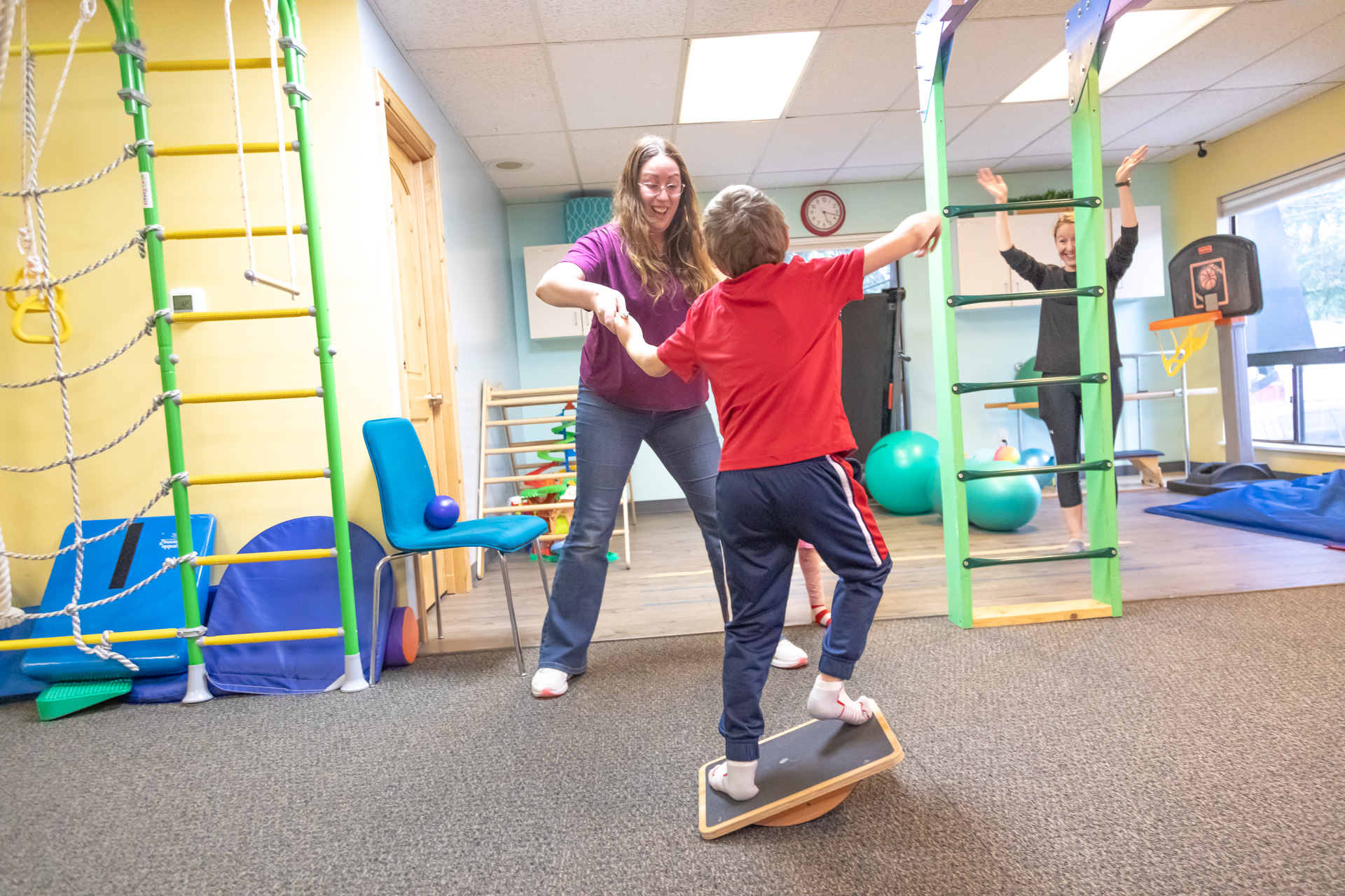 Child practicing balance on a therapy board with support from a physical therapist, building strength, coordination, and confidence through play-based pediatric PT.