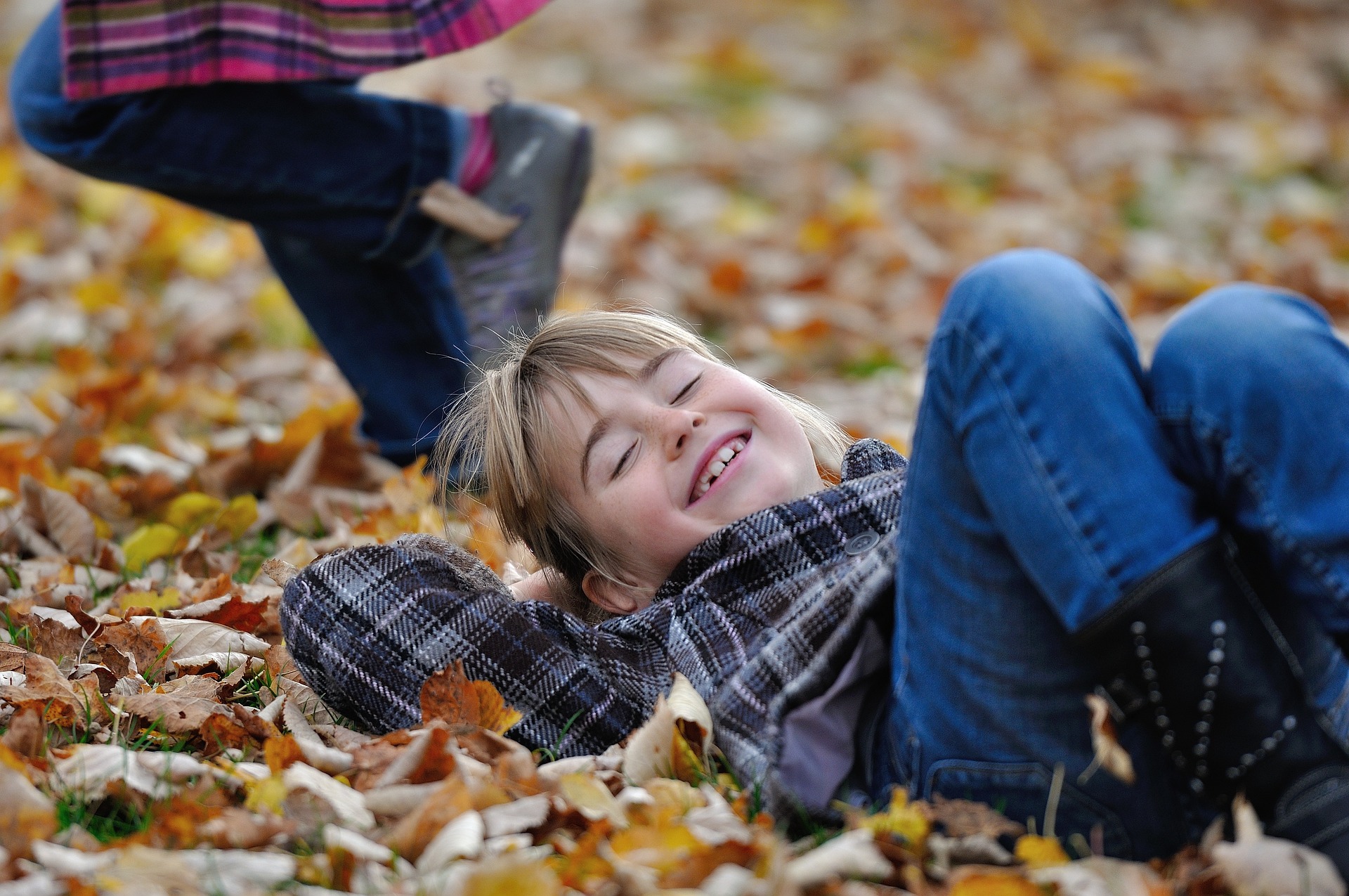 Child smiling while playing in autumn leaves, supporting social engagement, joyful interaction, and meaningful fall experiences.