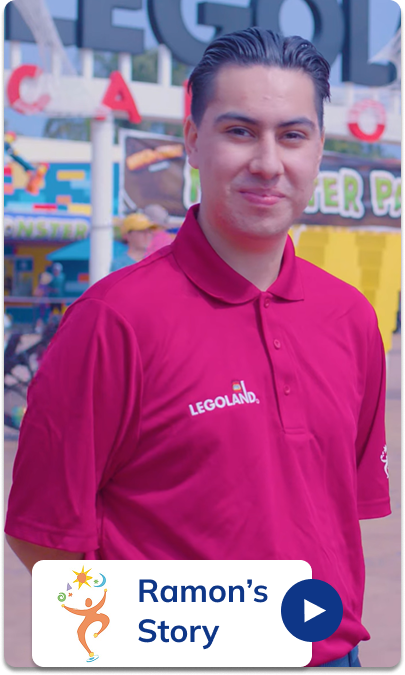 A smiling young man named Ramon wearing a bright pink LEGOLAND polo shirt, standing in front of a colorful LEGO-themed background. The is  from a video by the California Department of Developmental Services highlighting inclusive employment at LEGOLAND California.