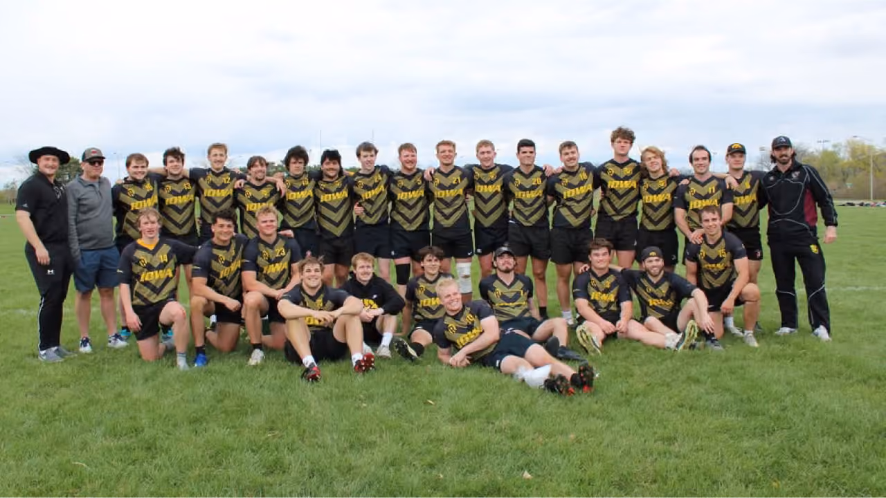 A rugby team wearing black and yellow Iowa jerseys posing together on a grassy field.