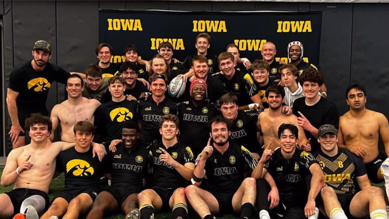 Group of male athletes wearing Iowa rugby uniforms posing for a team photo indoors on turf.