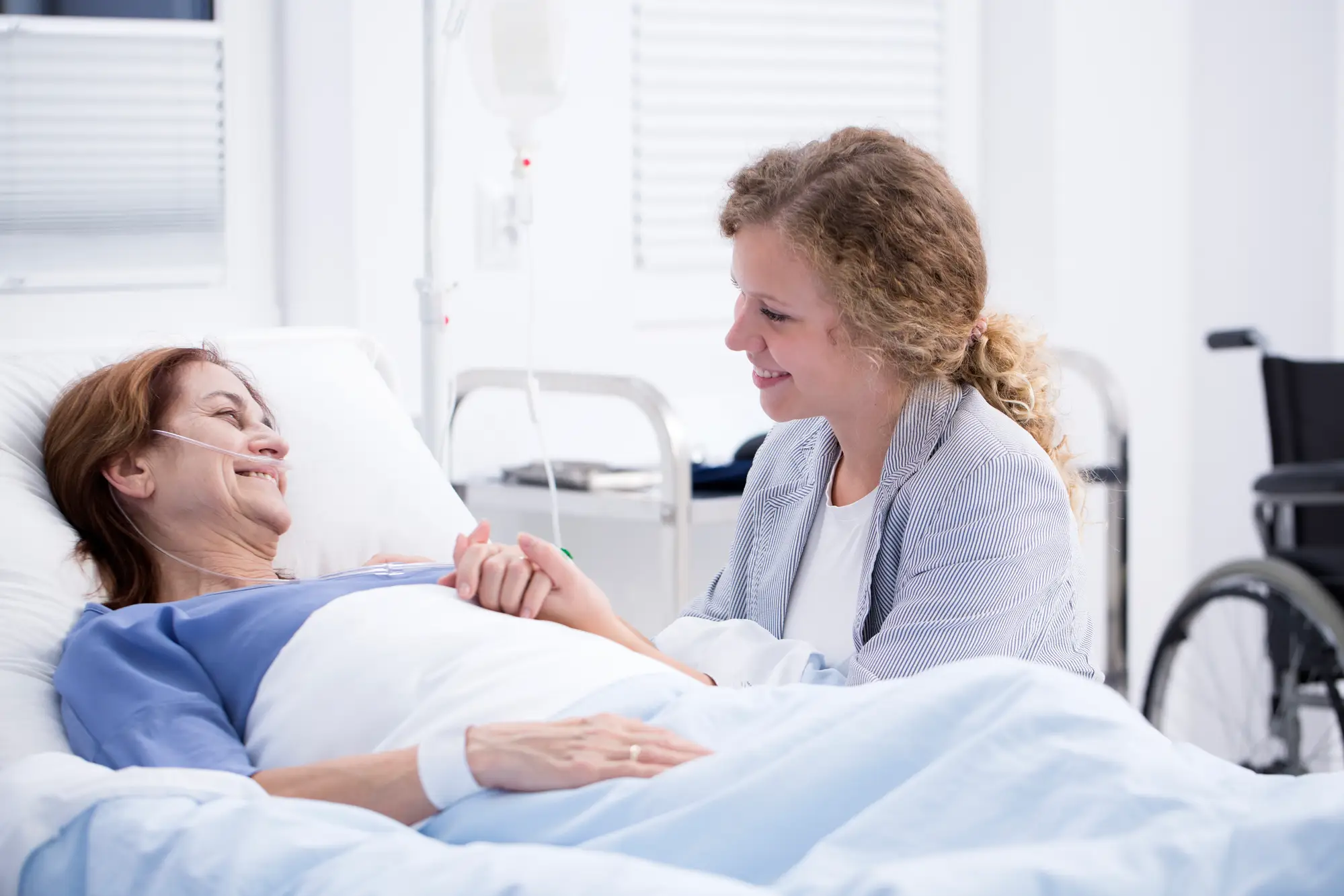 Spitex-Mitarbeiterin hält die Hand einer lächelnden Patientin im Spitalbett.