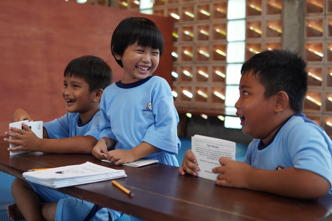 Drei Kinder in Schuluniform lachen gemeinsam im Klassenzimmer