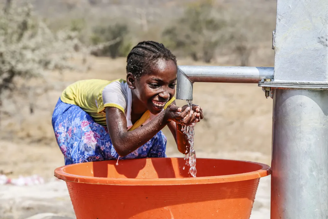 Mädchen wäscht sich lachend die Hände an einer Wasserpumpe