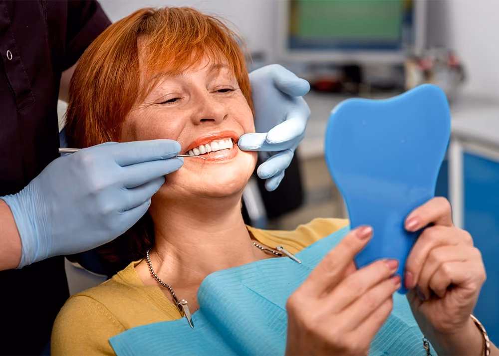 Middle-aged woman smiles at the mirror in a dentist’s chair, happy she has the best restorative dentist in San Francisco