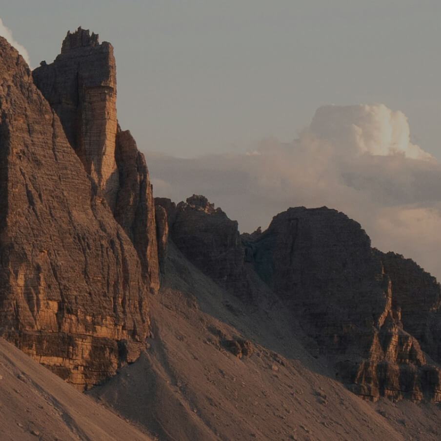 Sunlit rugged rocky mountain cliff with a cloudy sky in the background.
