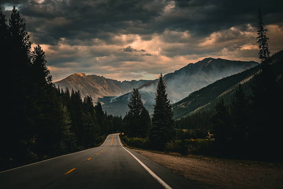 A winding river flowing through a forested valley with mist and low clouds partially covering the surrounding mountains.