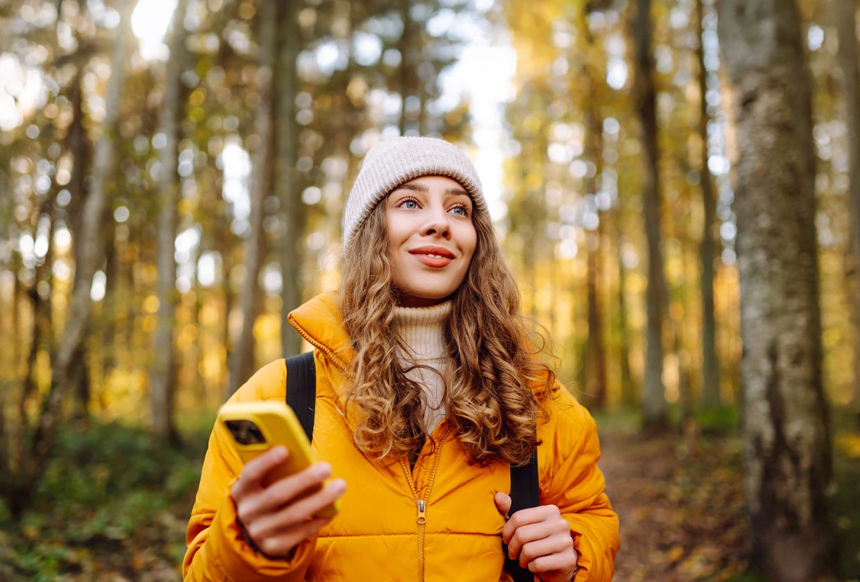 Femme souriante tenant un téléphone dans une forêt en automne