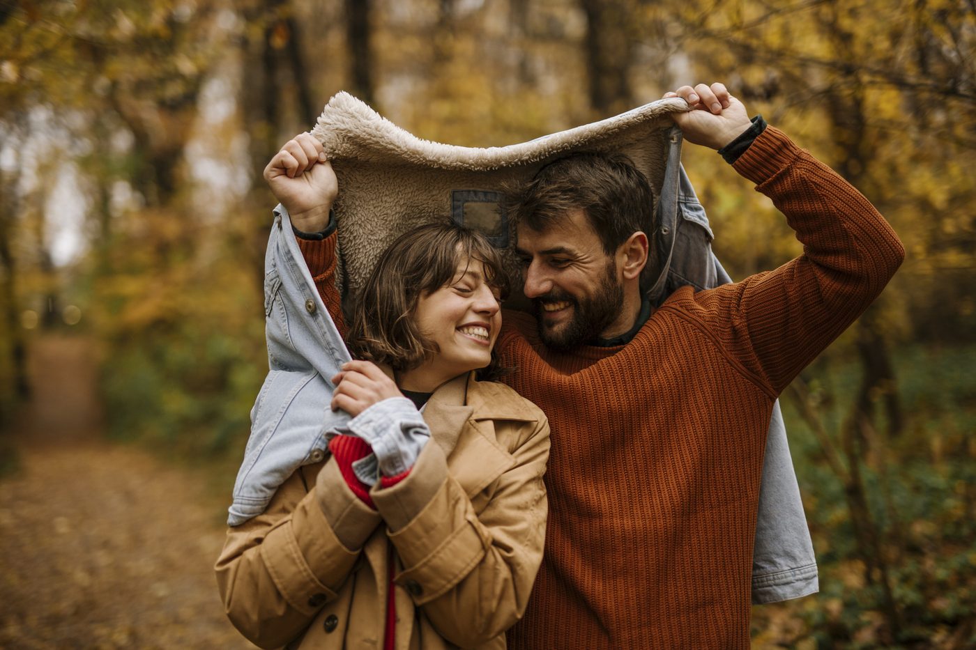 Un couple souriant s'abrite sous une veste lors d'une promenade en forêt en automne