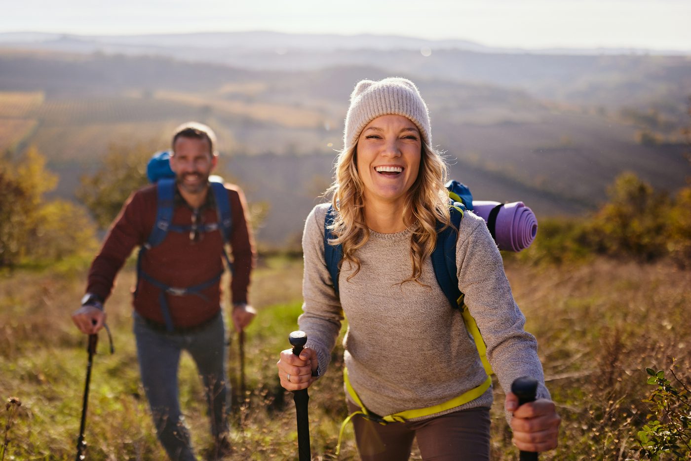 Deux randonneurs souriants, bâtons de marche en main, sur un sentier de colline