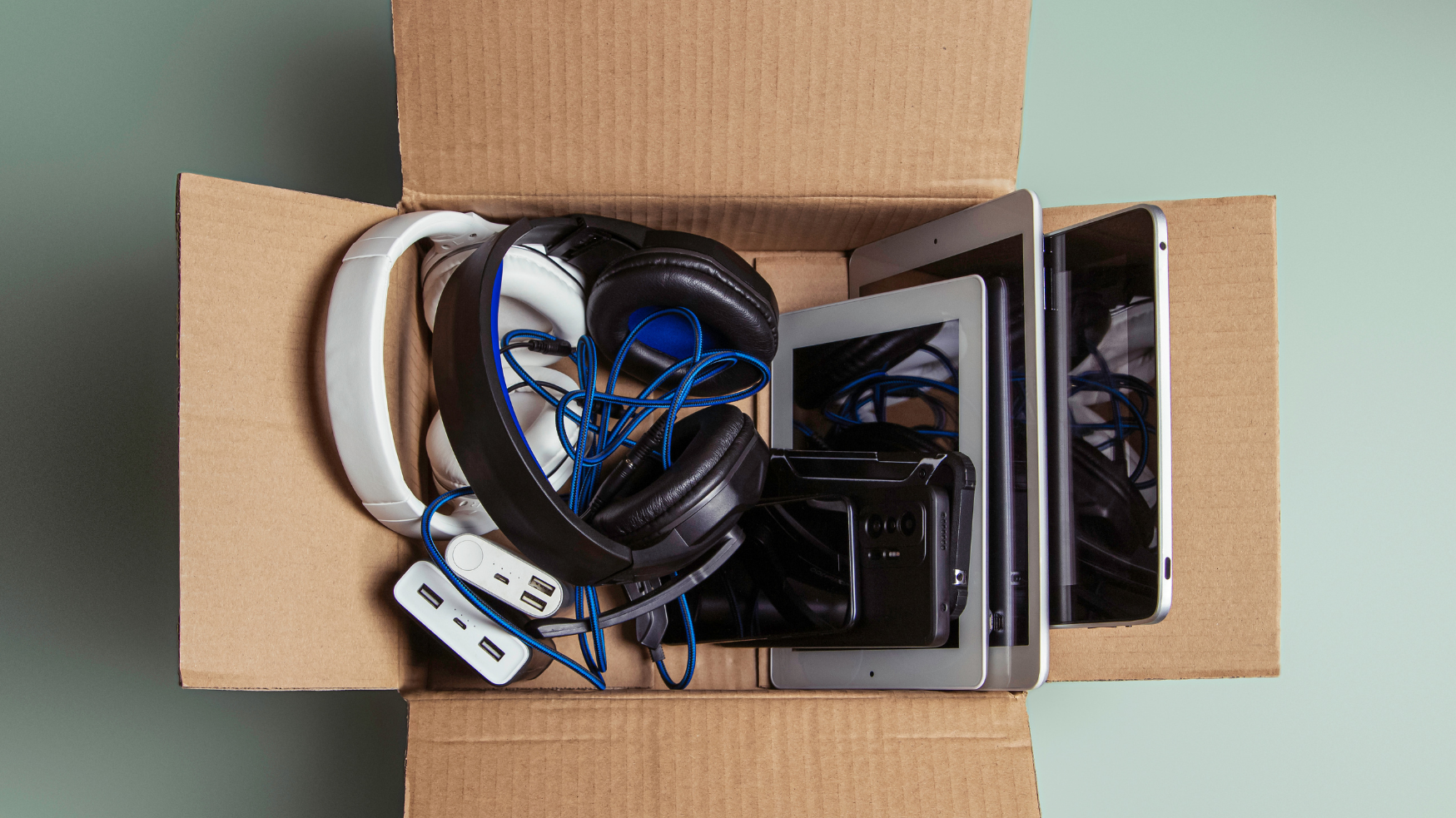 Carton contenant des tablettes, smartphones, casque audio et accessoires informatiques.