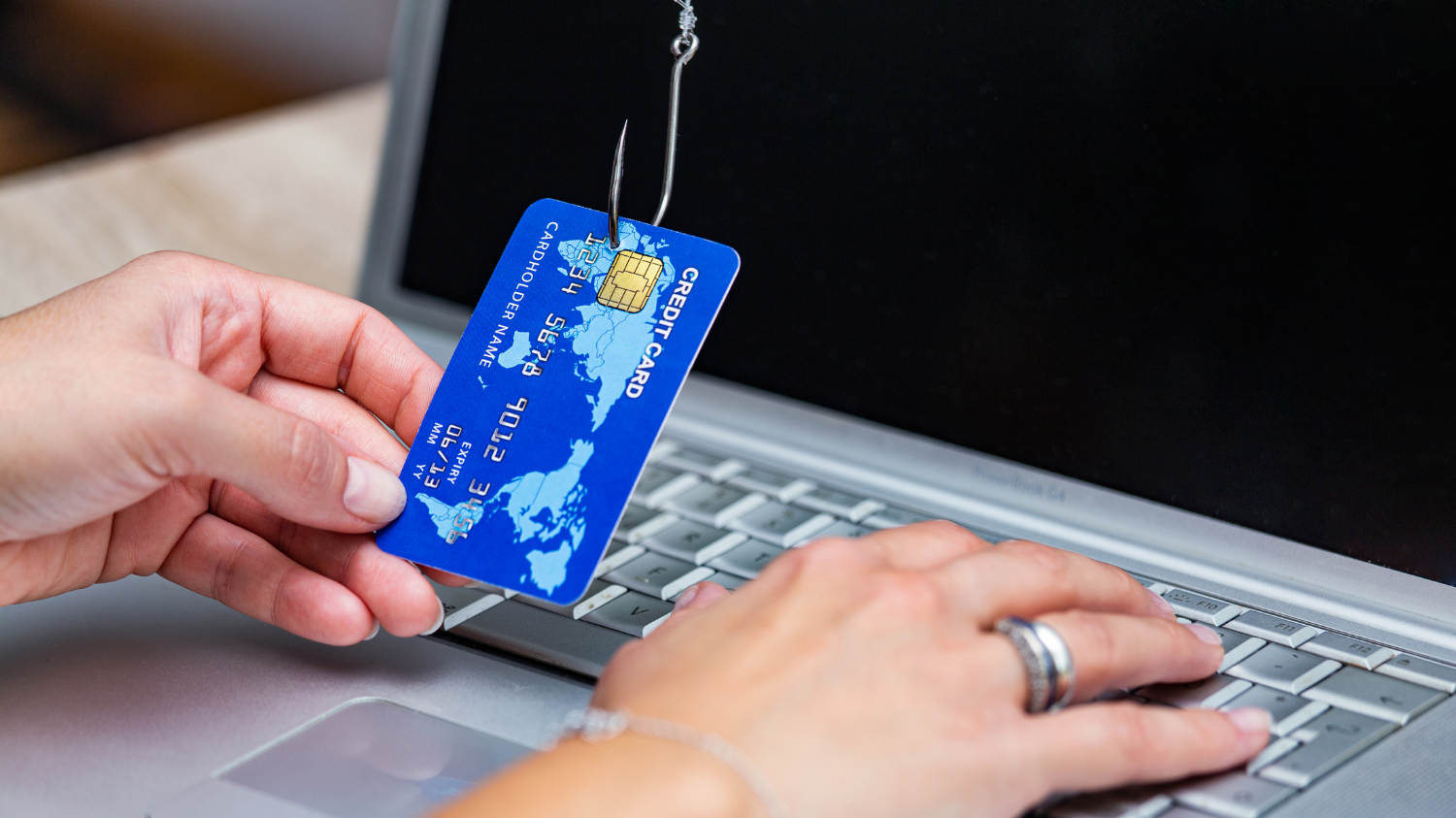 Carte bancaire accrochée à un hameçon devant un ordinateur portable.