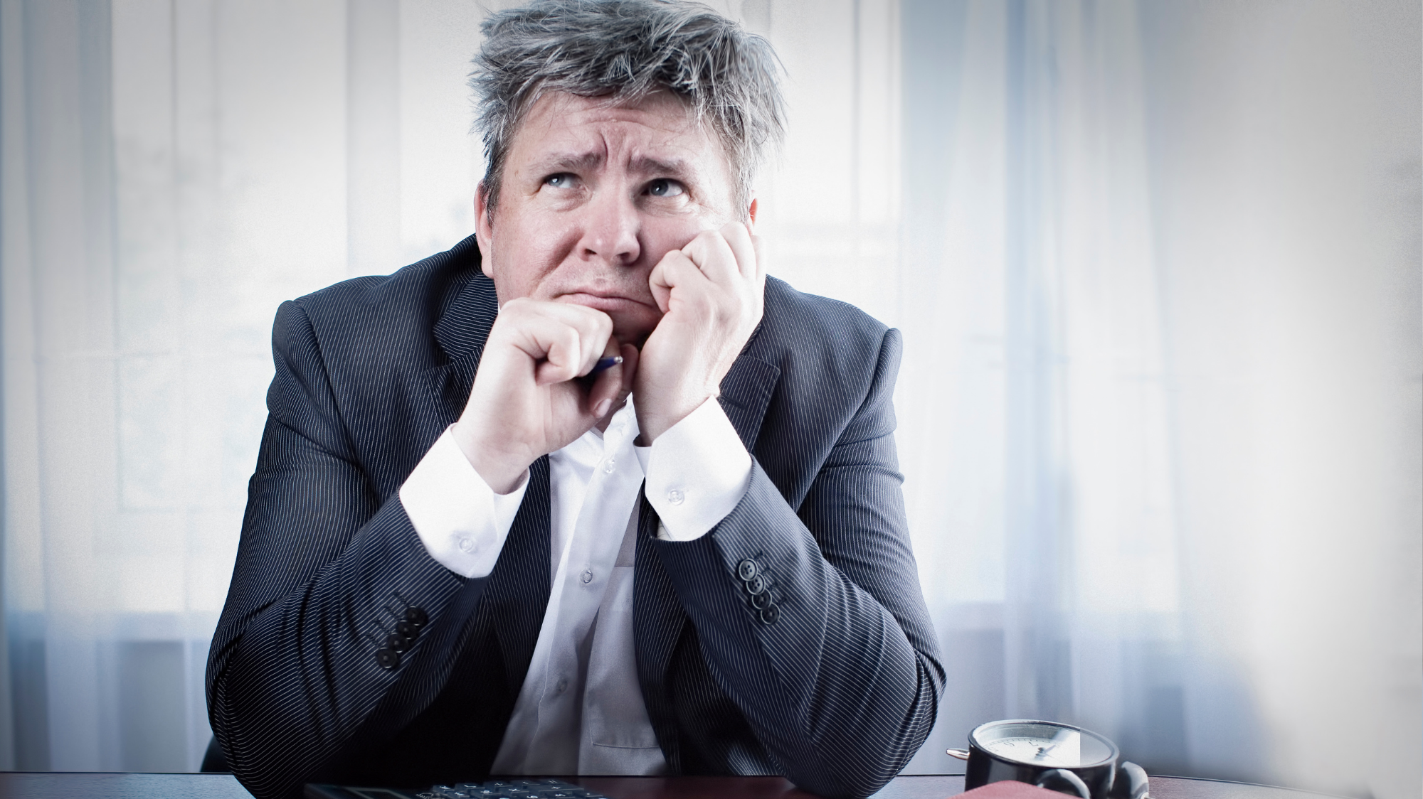Homme en costume réfléchissant, assis à un bureau, illustrant l'hésitation avant le renouvellement d'un parc informatique.