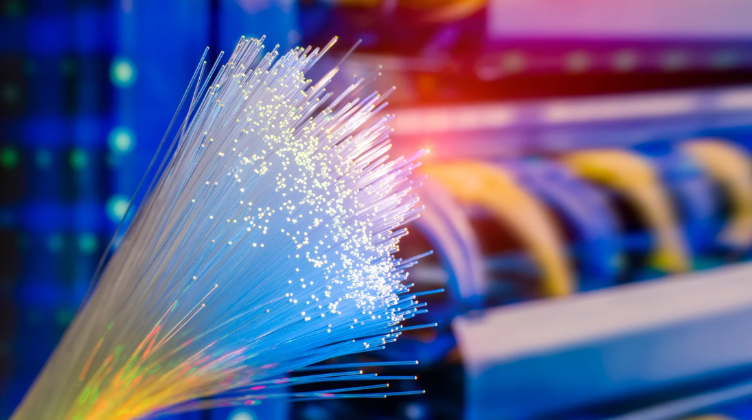 Gros plan sur des fibres optiques éclairées devant des équipements réseau dans une baie informatique.