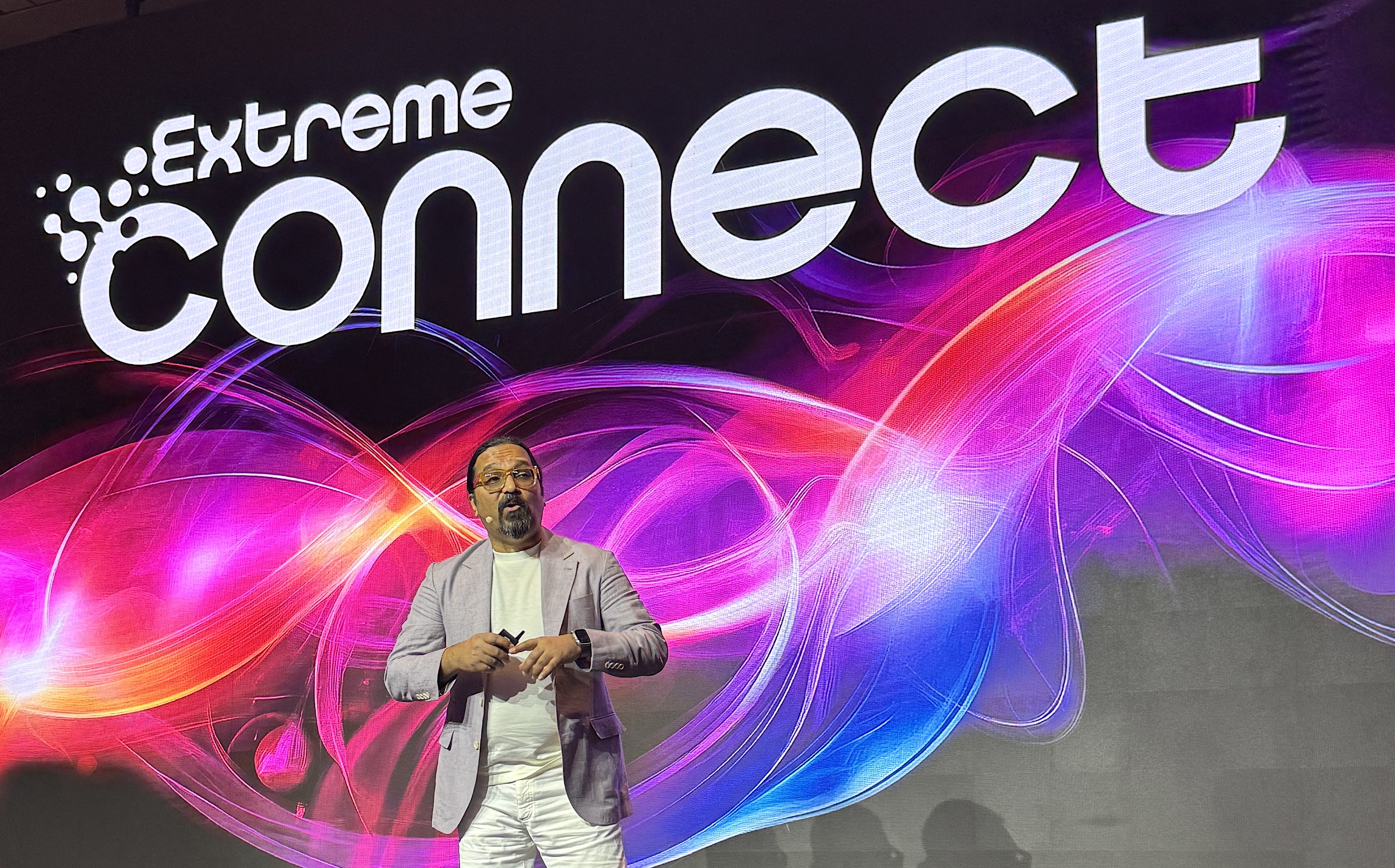 Intervenant sur scène devant un écran géant affichant le logo Extreme Connect et un visuel aux couleurs vives.
