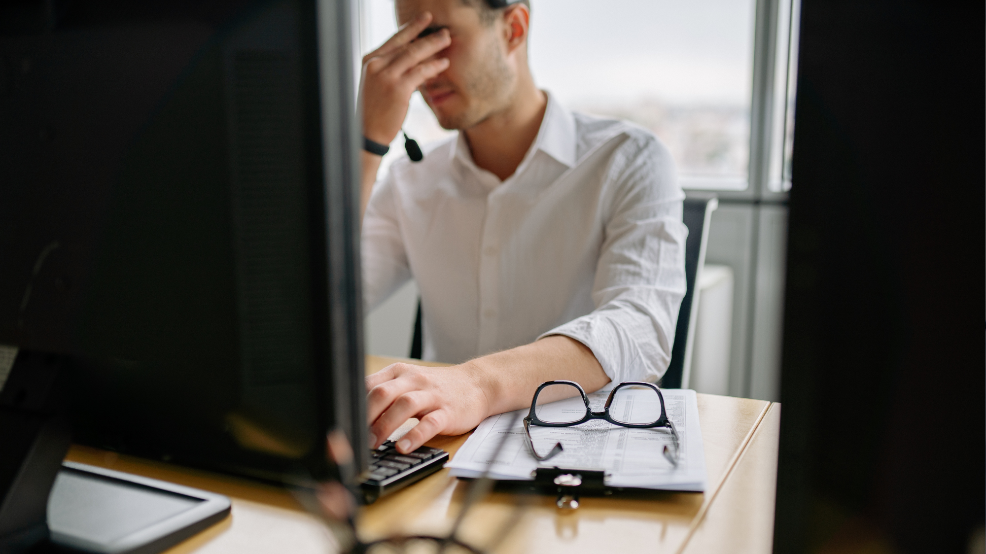 Employé portant un casque micro devant son ordinateur, manifestant une difficulté lors d'une intervention de support informatique.