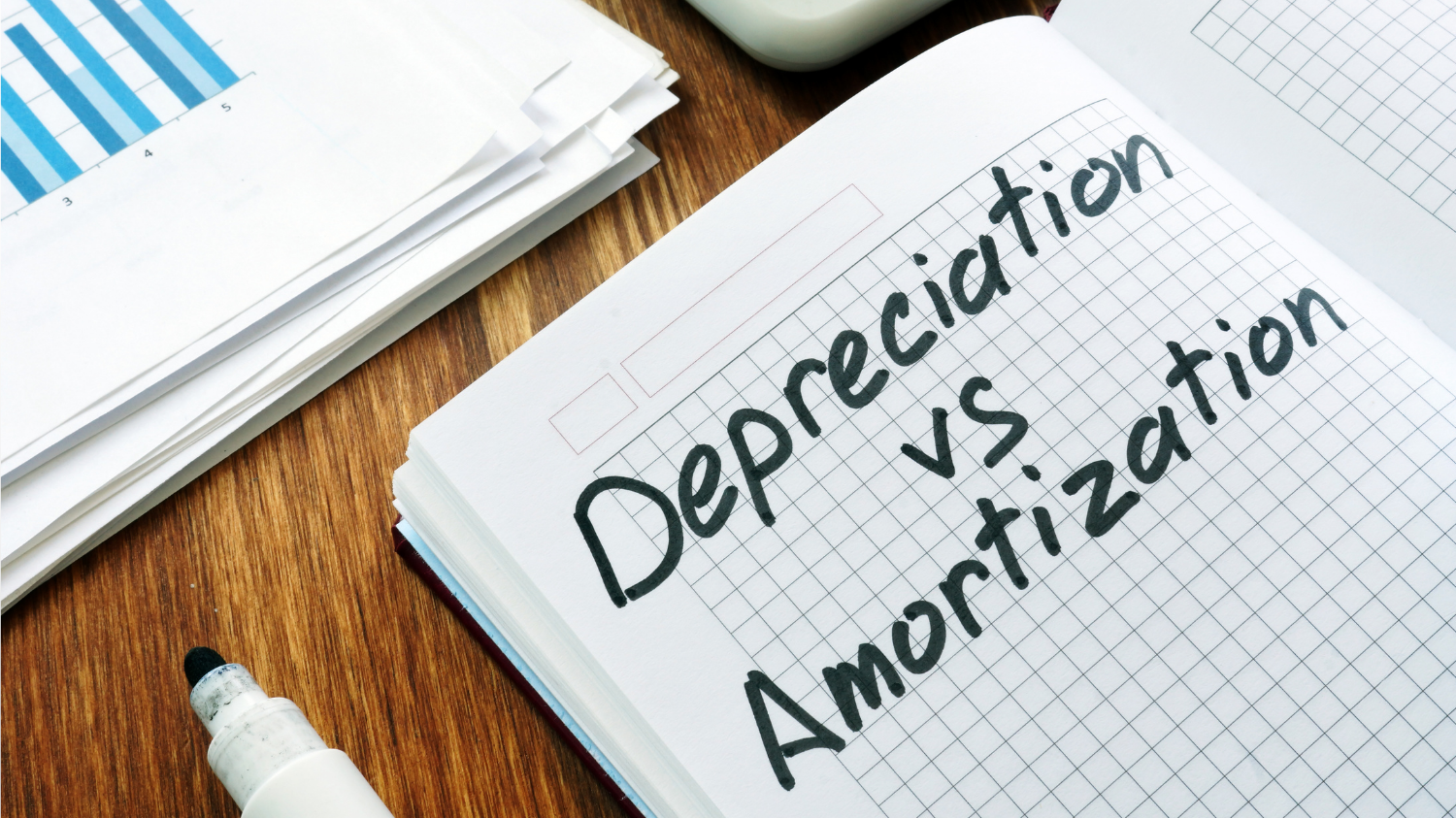 Carnet avec l'inscription « Depreciation vs. Amortization » à côté de documents financiers.