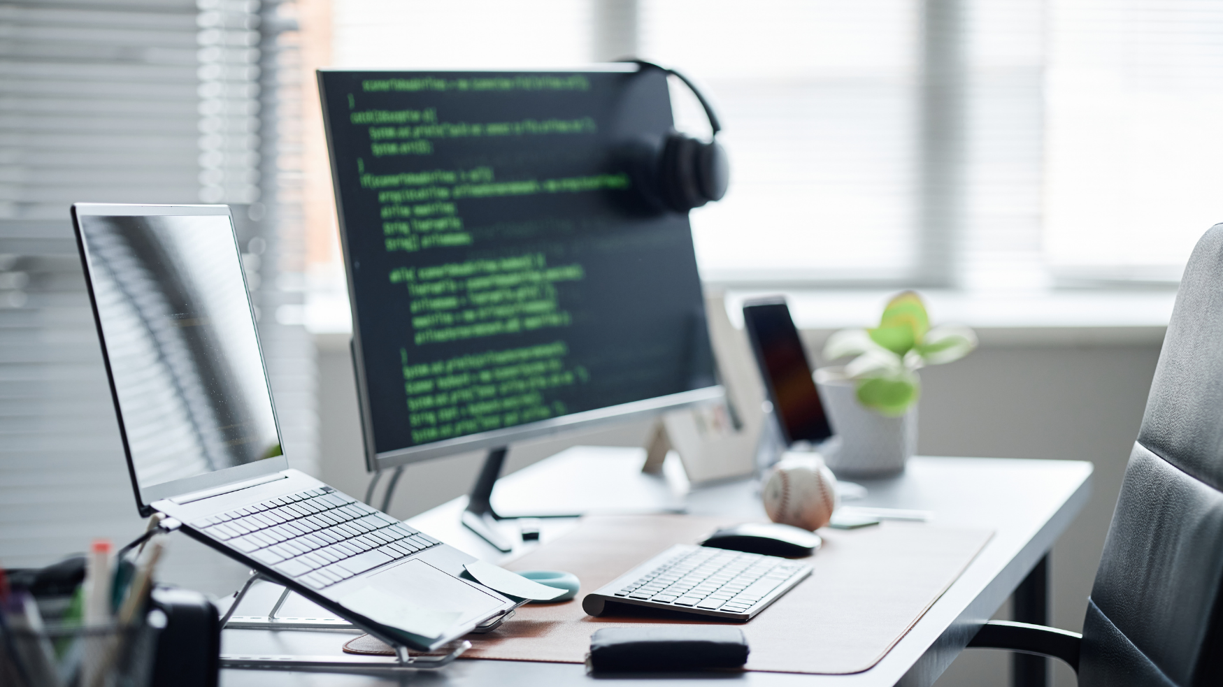 Poste de travail informatique avec ordinateur portable, écran affichant du code, clavier et smartphone sur un bureau.