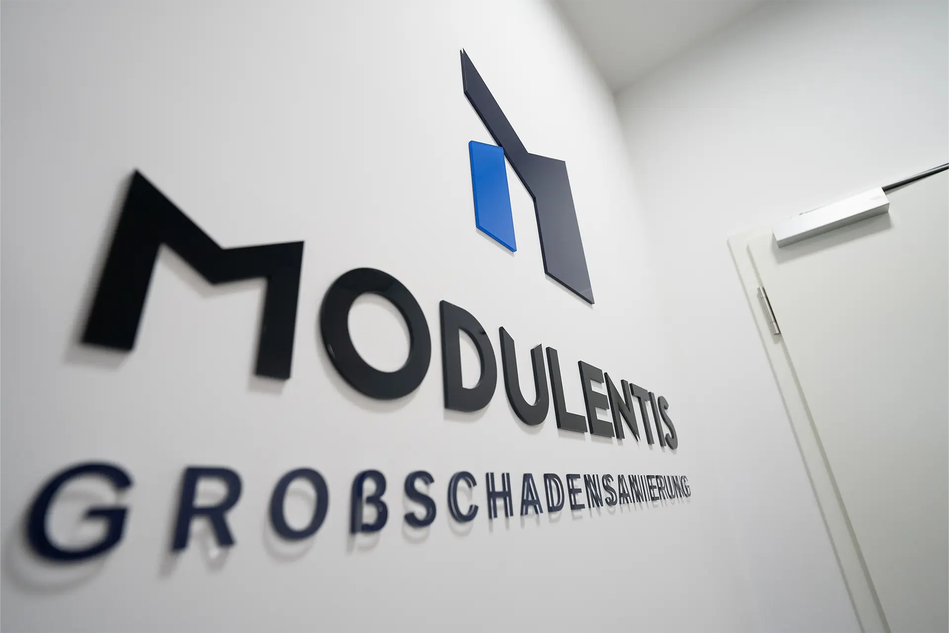 Das Logo von Modulentis Großschadensanierung an einer weißen Wand.