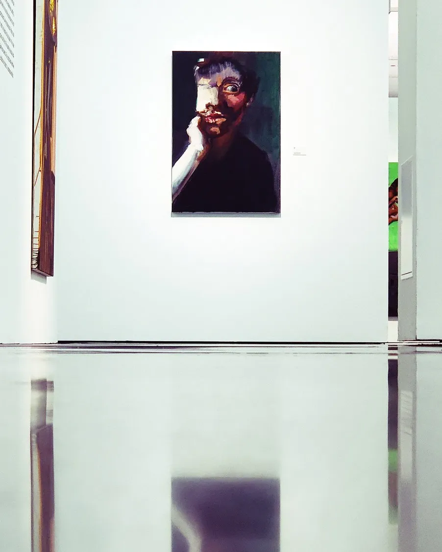 Abstraktes Porträtgemälde einer Person mit einem bedeckten Auge, ausgestellt an einer weißen Galeriewand mit Bodenreflexionen.