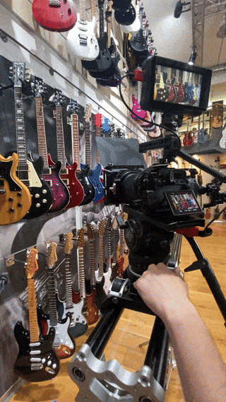 Eine auf einem Stativ montierte Kamera filmt eine Wandausstellung mit verschiedenen E-Gitarren in einem Musikgeschäft.
