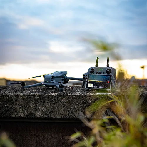 Kompakte Drohne und Fernbedienung mit Bildschirm ruhen bei Sonnenuntergang auf einem Betonvorsprung.