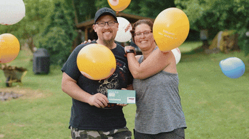 Lächelnde Personen freuen sich und feiern mit dem Glücks LOS der Aktion Mensch und Luftballons.
