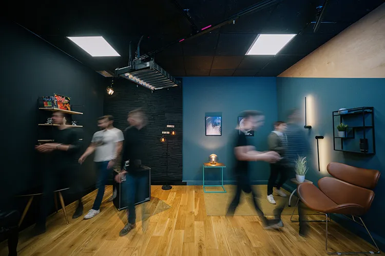 Verschwommene Bewegung von sechs Personen, die durch einen modernen Studioraum mit dunklen Wänden, Holzboden und minimalistischen Möbeln gehen.