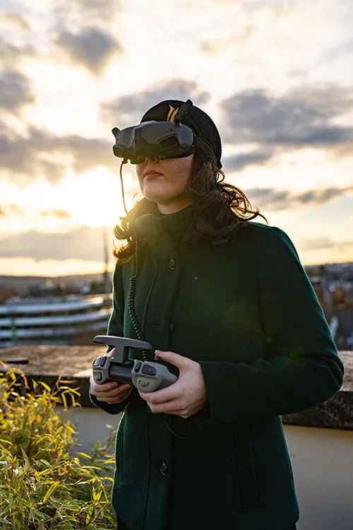 Person mit FPV-Brille und Drohnenfernsteuerung im Freien bei Sonnenuntergang.