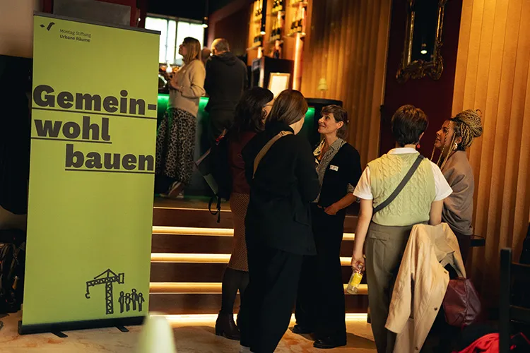 Eine Gruppe von Menschen unterhielt sich in der Nähe einer beleuchteten Treppe und eines grünen Banners in einem warm beleuchteten Raum.