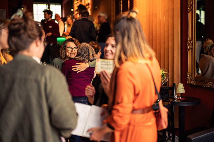 Menschen umarmen sich und unterhalten sich in einem warm beleuchteten Raum bei einer geselligen Veranstaltung.