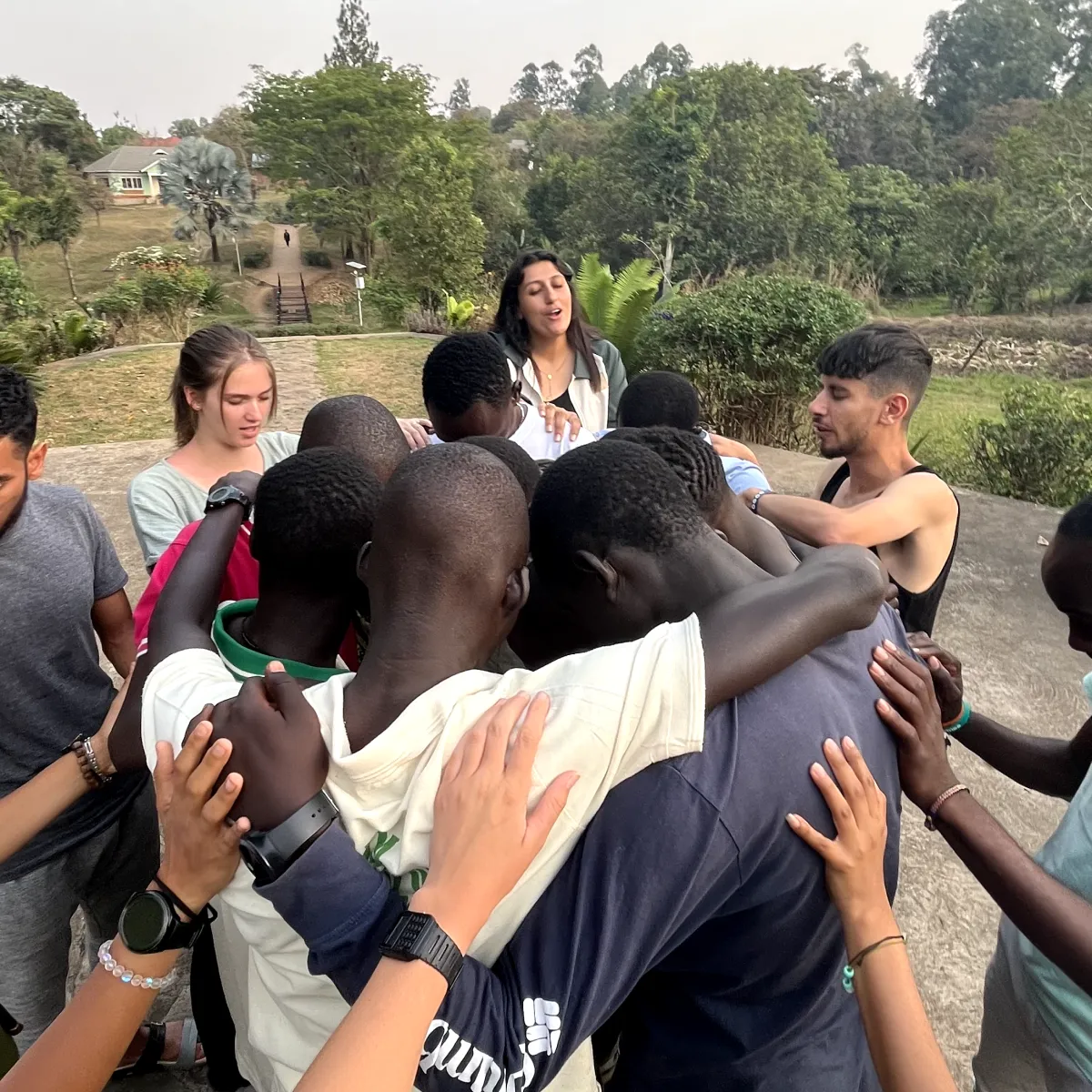 A group of students praying around a group of children with their arms around each other.