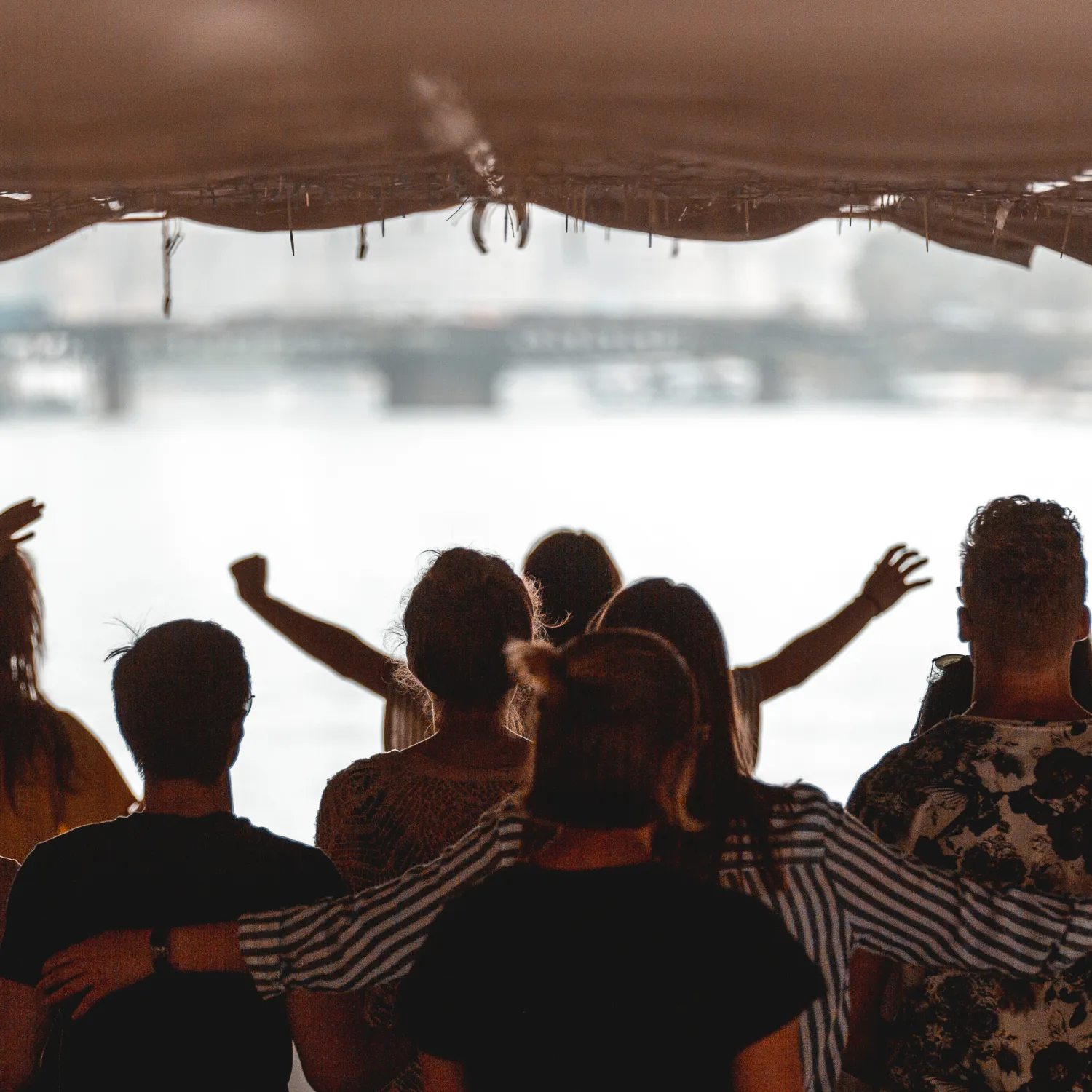 A group of students under a tent worshipping with their arms out.