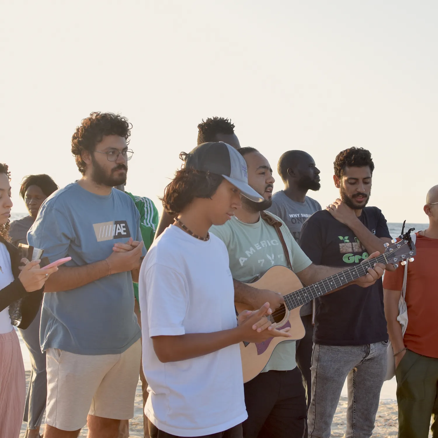 A group of students standing and worshipping with one student playing the guitar.
