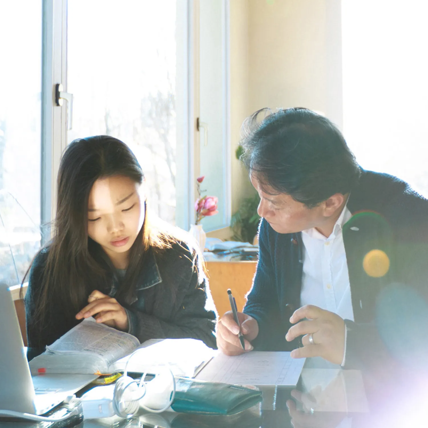 Two students seated at a desk together and looking down at their notes.