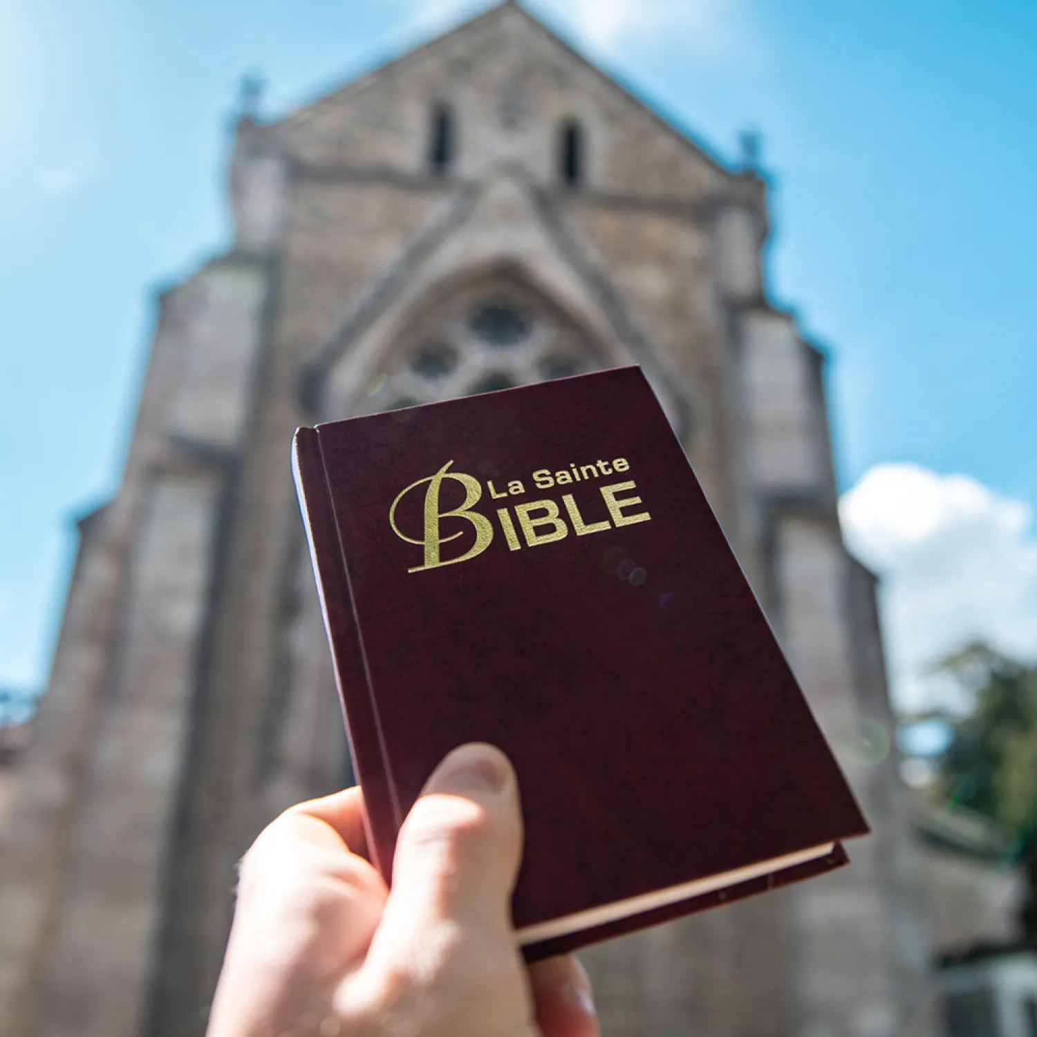 A hand holding a Bible in front of a church.