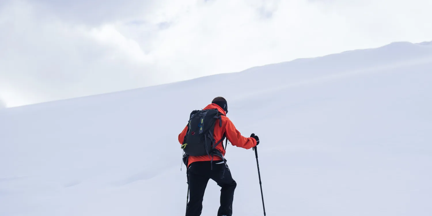 A man in a red jacket hiking up a hill of white snow during the winter DTS at YWAM Lausanne.