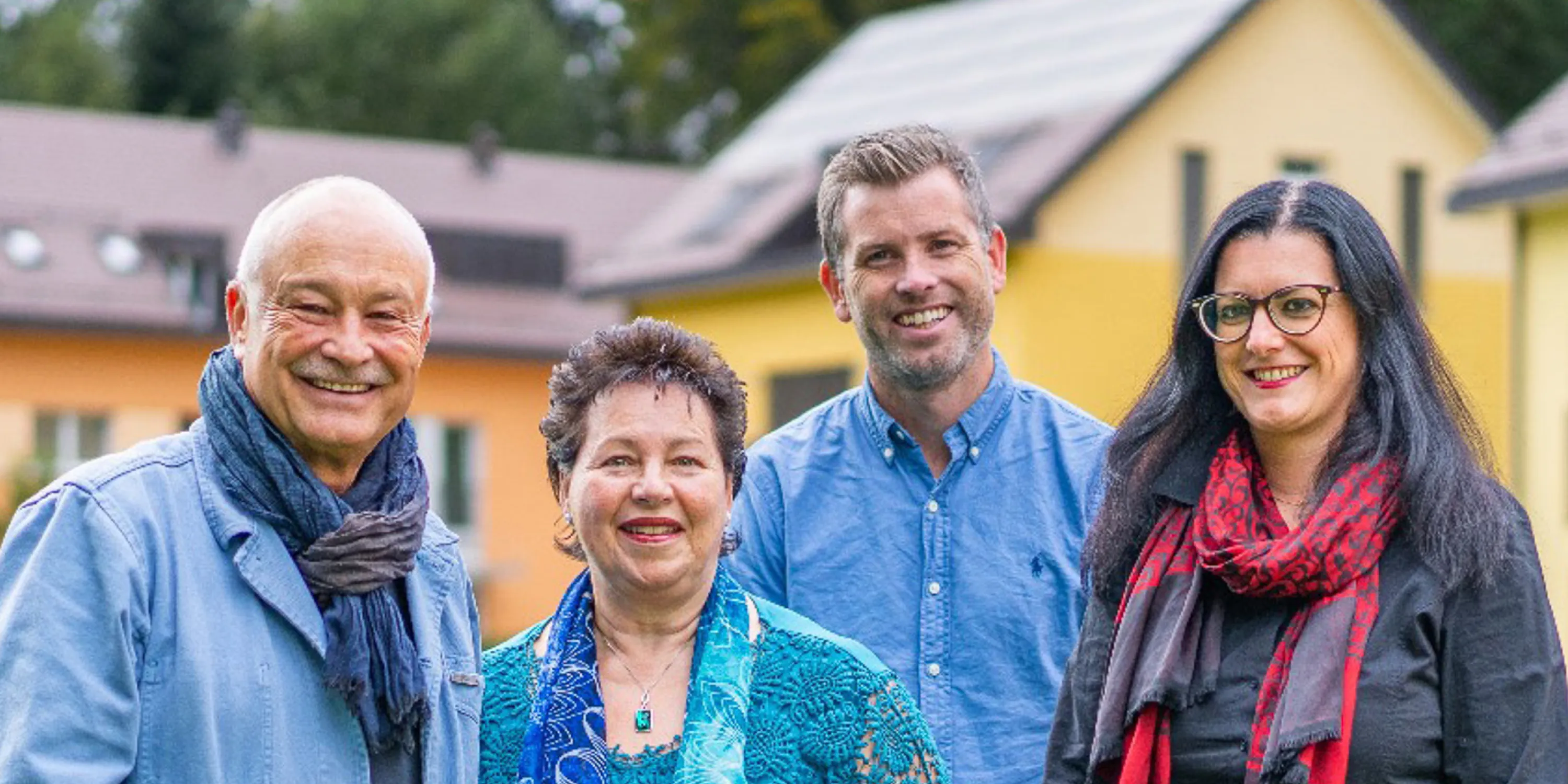 An image of four staff members standing and smiling in front of the YWAM campus building.