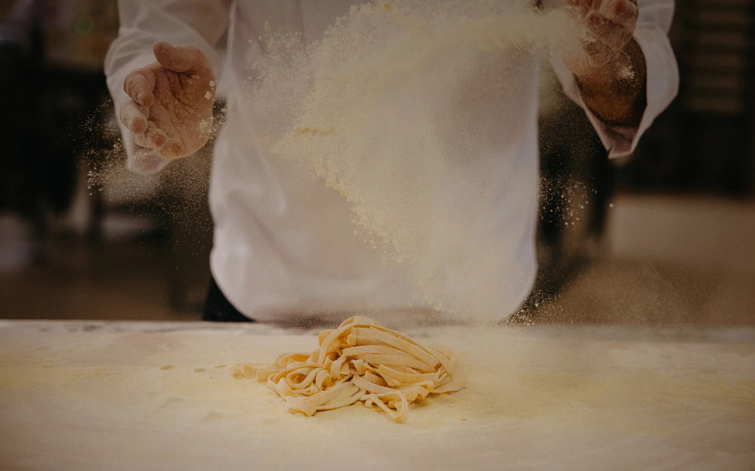 Hands sprinkling flour over fresh pasta dough on a floured surface.