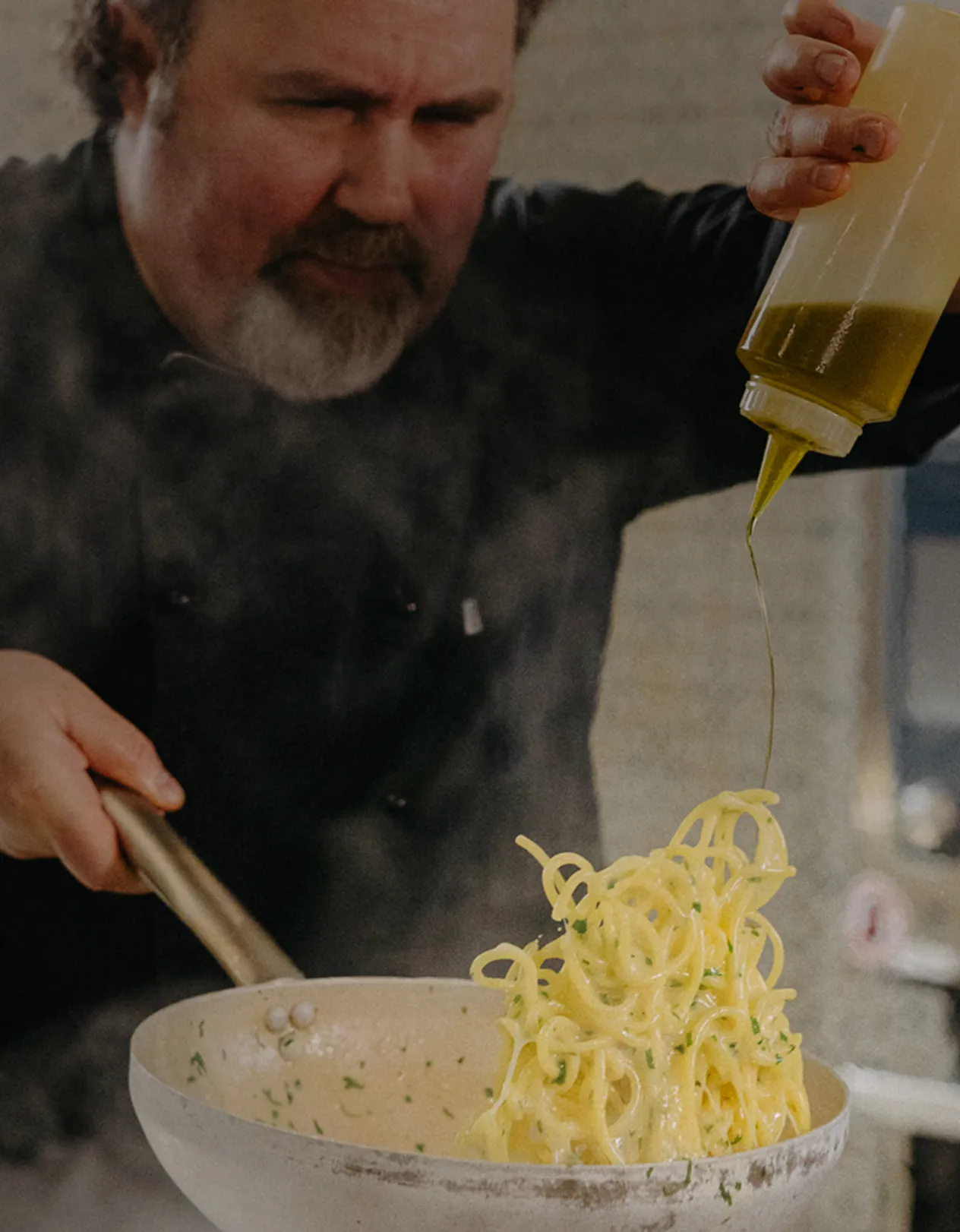 Lo chef getta gli spaghetti in padella mentre irrora l'olio d'oliva.