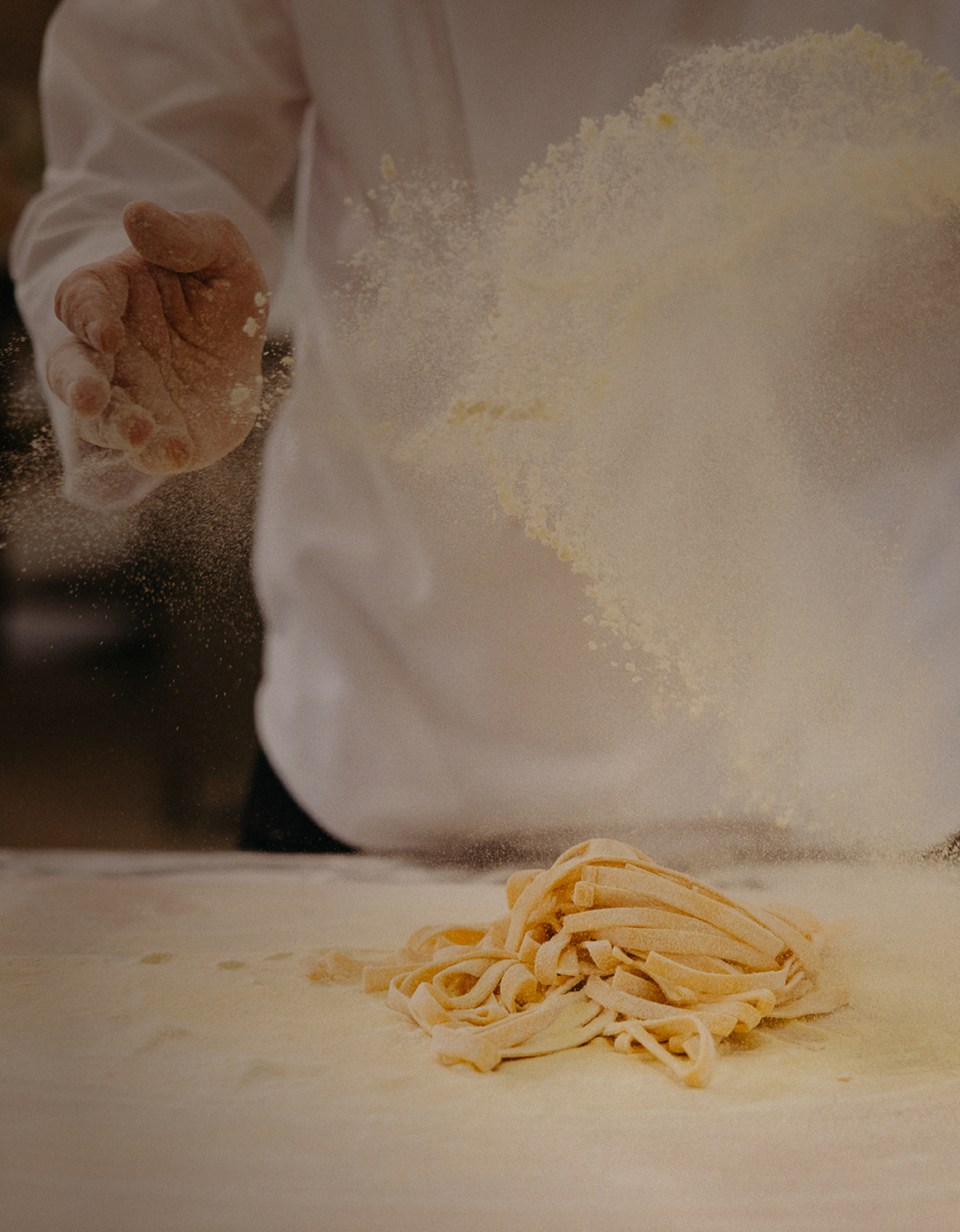 Hands sprinkling flour over fresh pasta dough on a floured surface.