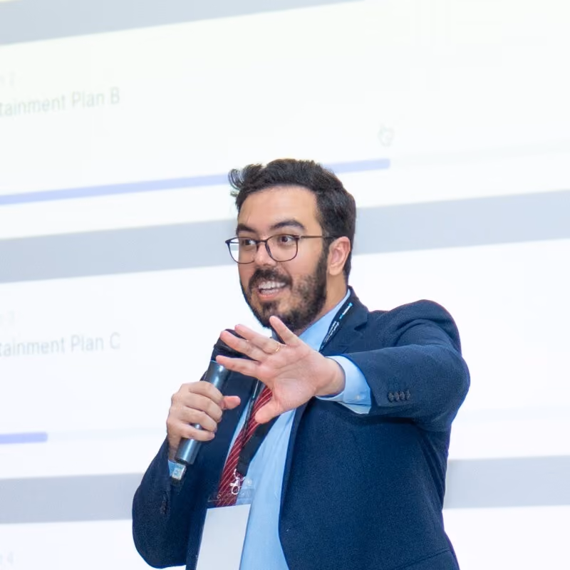 Man in glasses and suit speaking into microphone while gesturing with hand at a presentation.