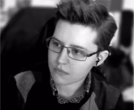 Black and white portrait of a person with short hair wearing glasses and an earbud, looking slightly to the left.