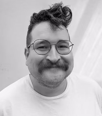Black and white portrait of a smiling man with round glasses, a mustache, and tousled hair wearing a light-colored shirt.