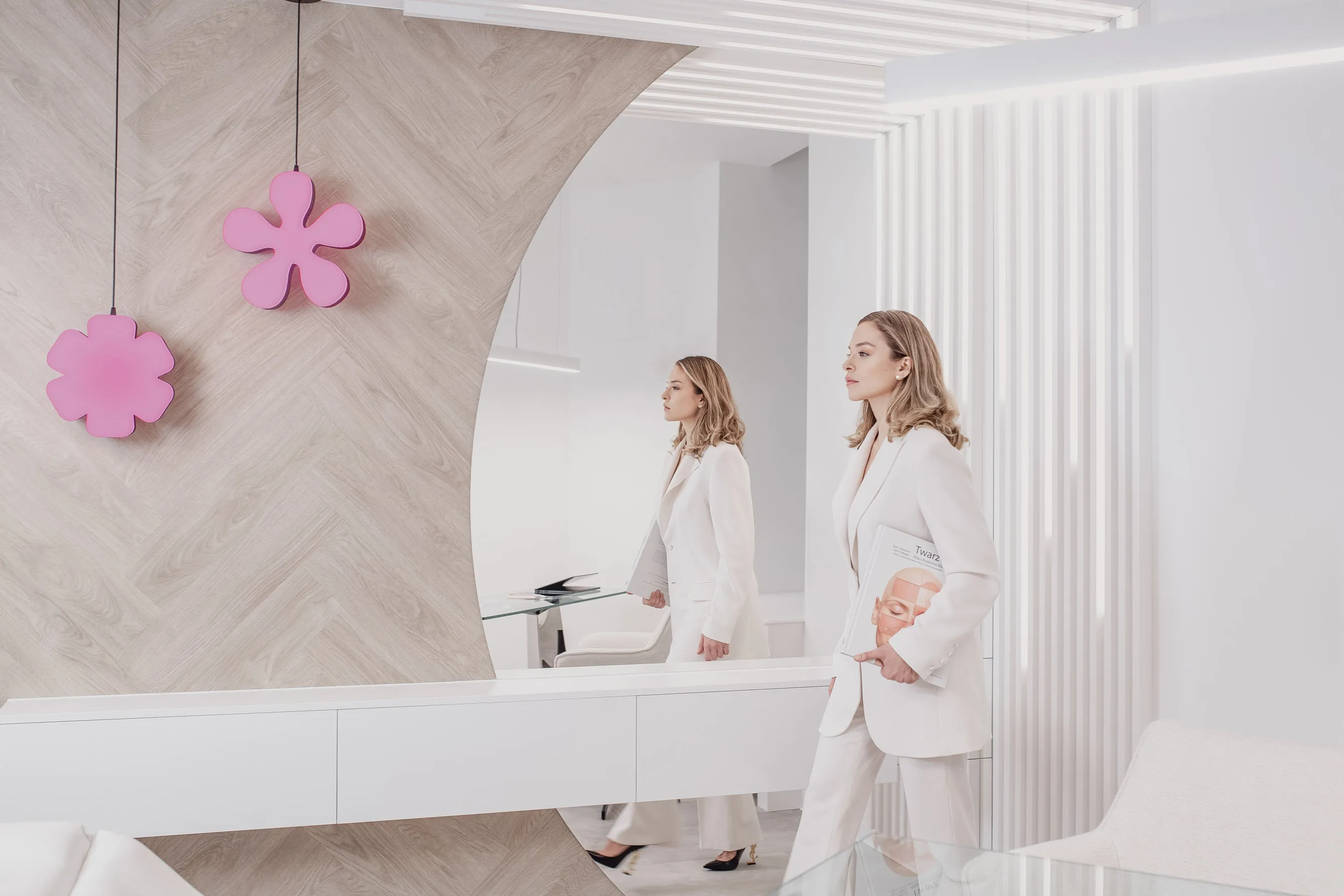 A woman in a white suit walks through a modern, minimalist office holding a magazine.